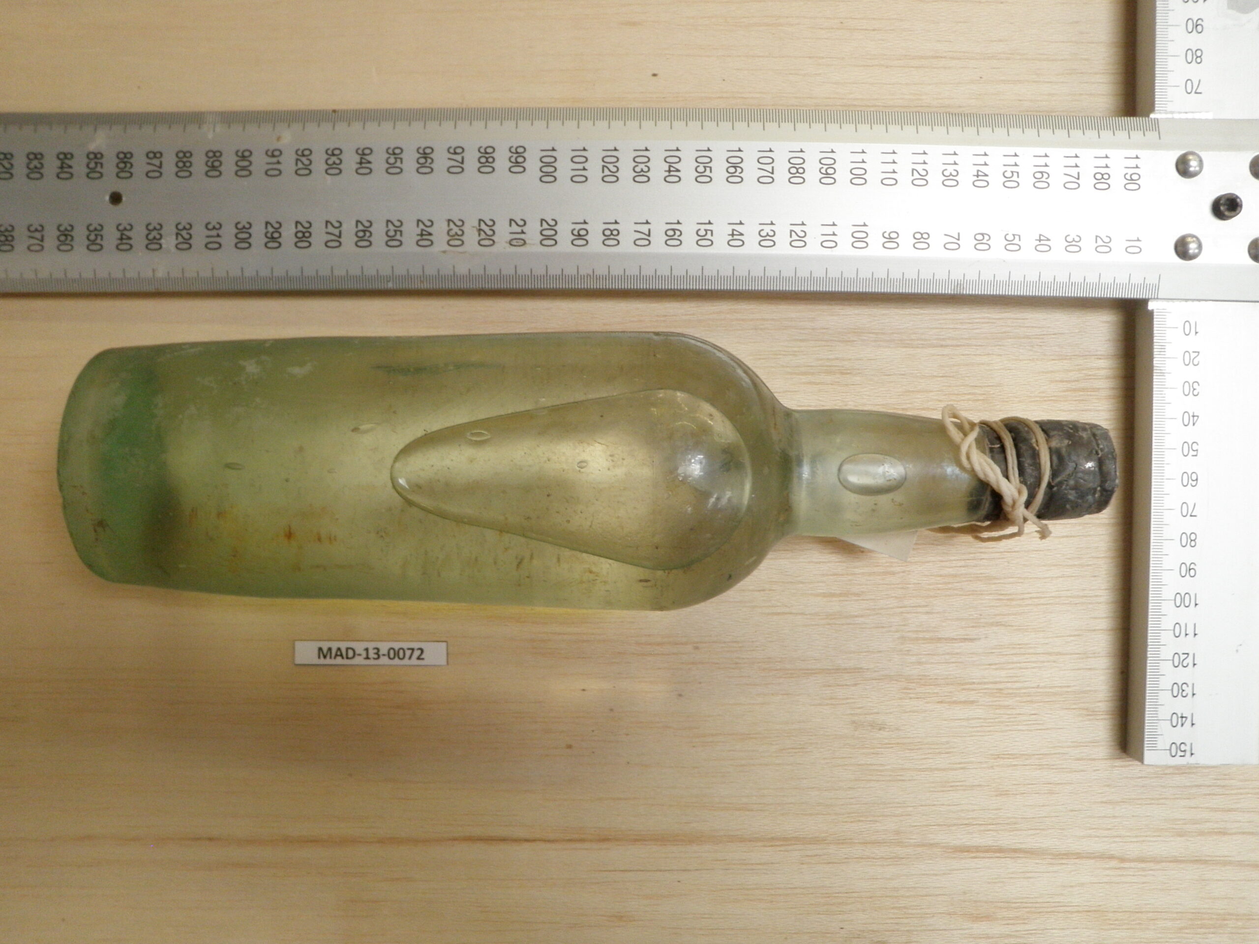 Conservation documentation photograph of SS Mantola gin bottle MAD-13-0072 with metric scale rulers